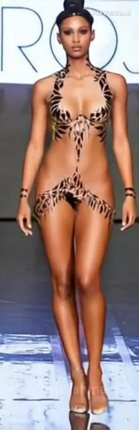 Model with black and gold body paint, styled as a bikini, walks down a fashion show catwalk.