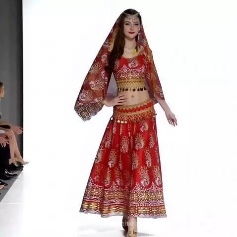 Female model in a vibrant red two-piece outfit with gold patterns walks down a white catwalk at a fashion show.