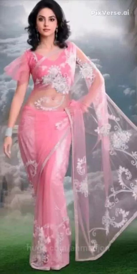Model with dark curly hair wearing a sheer pink floral embroidered saree and ruffled blouse, posing against a cloud and grass backdrop.