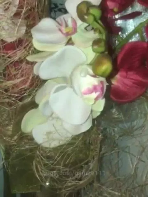 Close-up of a decorative floral arrangement with white, pink, and red artificial orchids in a straw-like base.