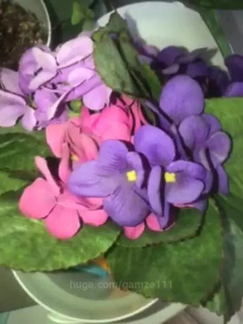 Close-up of a vibrant bouquet of artificial purple and pink flowers with green leaves in a white pot.
