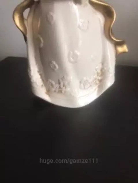 Close-up of a ceramic angel figurine with blonde hair, white dress with gold accents, holding a golden heart.