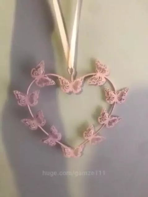 Close-up of a heart-shaped ornament formed by small, detailed butterflies, suspended by a ribbon.