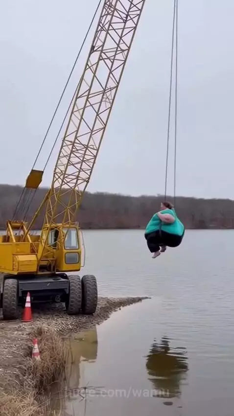 A yellow crane boom bends and snaps, causing a person on a swing to fall into the water below.