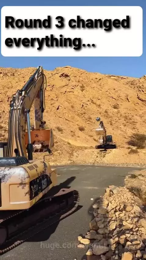 A large excavator in the foreground launching a dark spherical object into the air against a backdrop of arid mountains.