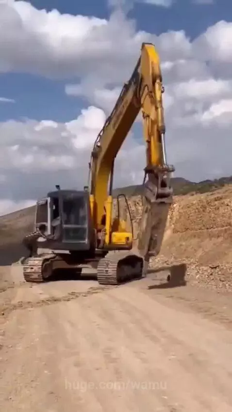 Man in plaid shirt narrowly avoids excavator arm on a dirt road construction site.