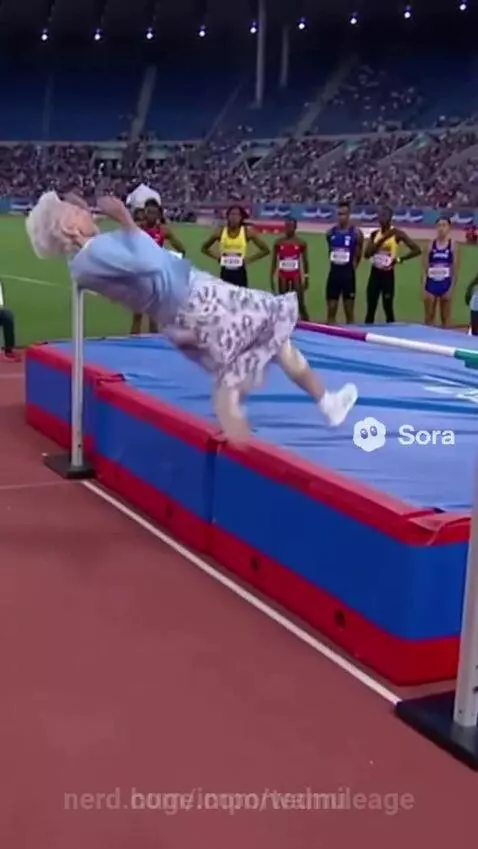 Elderly woman in blue sweater and patterned skirt successfully clearing a high jump bar in a stadium.