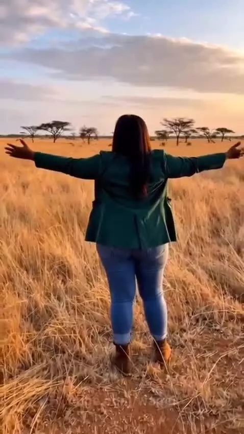 A large male lion hugs a woman from behind on a savanna during sunset.