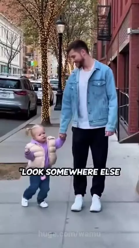 A child holds a man's hand on a city sidewalk, looking off-camera with a playful expression.