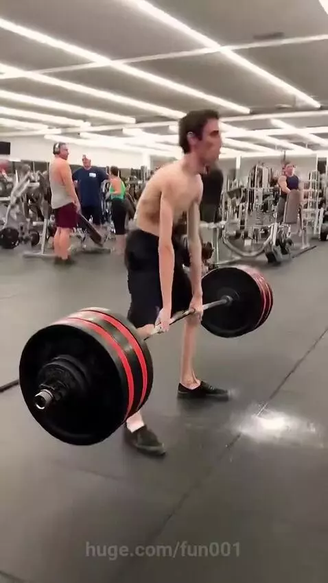 Thin man deadlifting a heavy barbell in a gym, surprising onlookers with his strength.