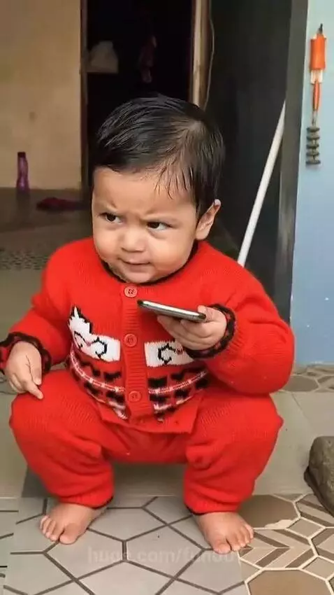 Baby in red sweater squatting, then dancing happily to music while holding a smartphone.