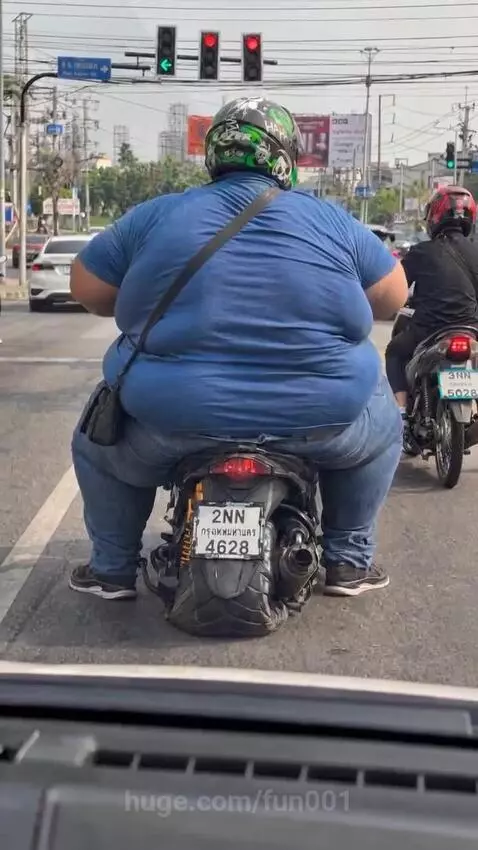 Overweight man falling off a scooter after it spins out at a traffic light.