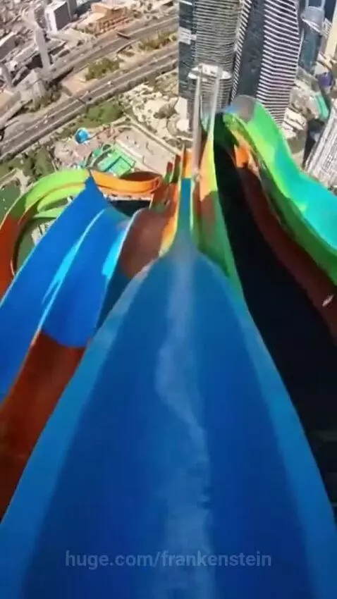 First-person view of a person riding a high, colorful water slide with a city skyline in the background.