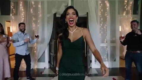 Woman in an elegant green dress enters a decorated party room with fairy lights and rose petals, smiling joyfully.