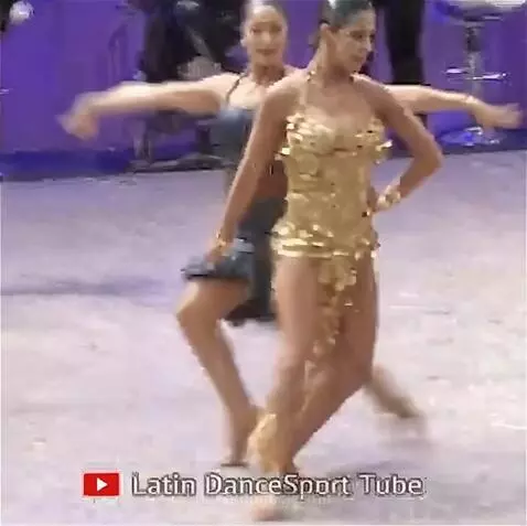 Two women performing a vibrant samba ballroom dance, one in a gold sequined dress.