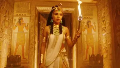 Young woman dressed as an ancient Egyptian princess holding a torch, exploring a tomb with hieroglyphs.