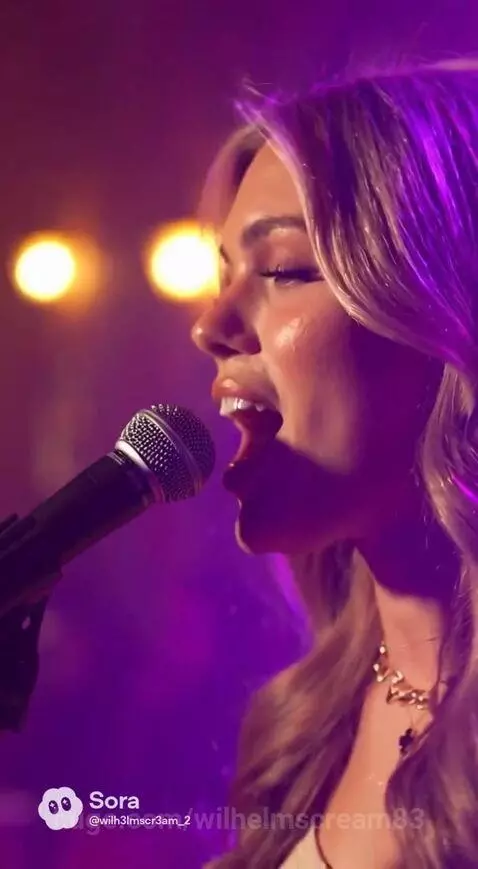 Woman with blonde hair singing on stage with desert screen backdrop and darbuka drummer.