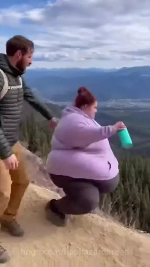 A large woman slides down a dusty mountain slope with a man looking on in alarm.