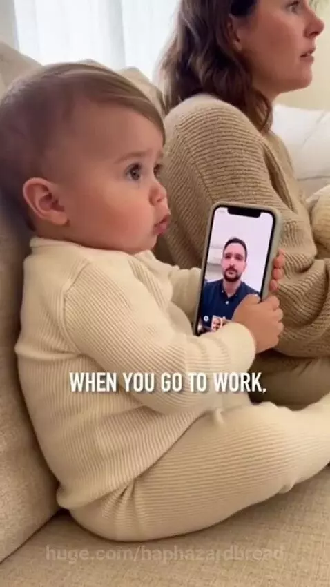 Baby on a couch holding a smartphone, video calling, with a woman partially visible next to him.