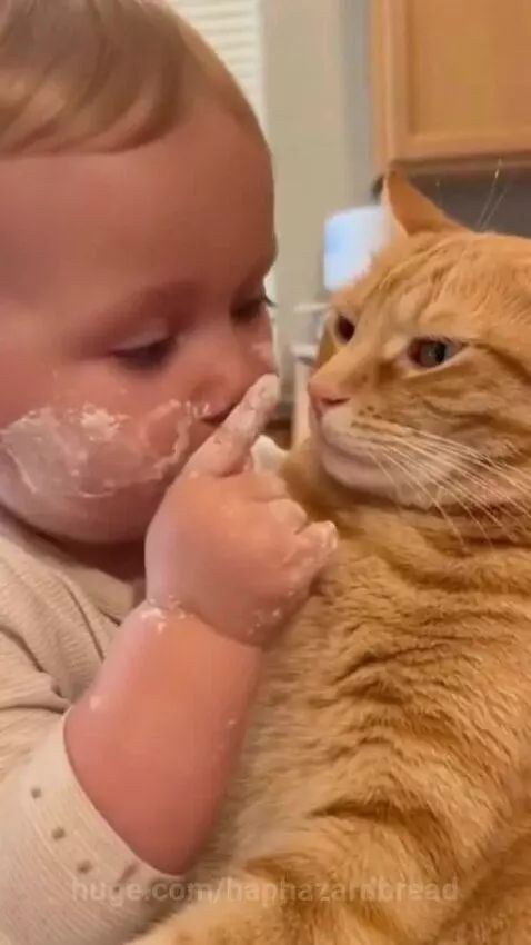 Baby with flour on face gently touching and kissing an orange cat's cheek.