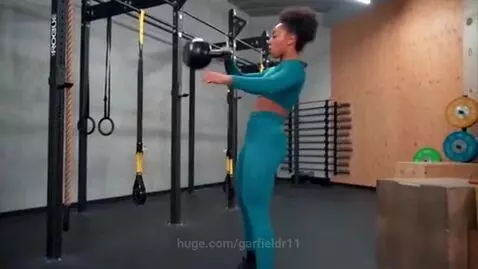 Woman with dark curly hair in teal athletic wear performing kettlebell swings in a gym.
