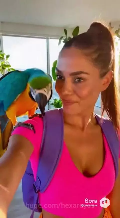 Woman dressed as Dora the Explorer with a blue and yellow macaw parrot on her shoulder, smiling indoors.