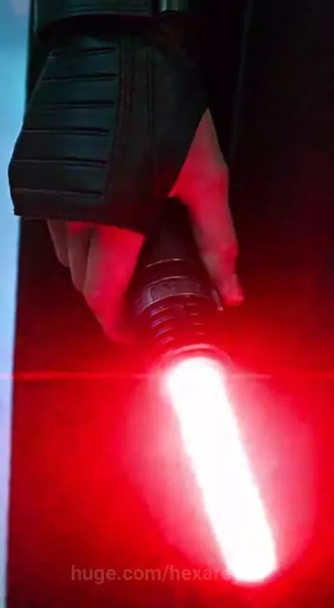 Hooded figure with red scars ignites a red lightsaber, menacing terrified children in a grand hall with a city skyline.