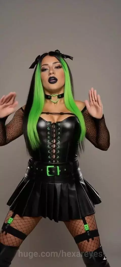 Woman with black hair and neon green streaks dancing suggestively in a black corset and fishnet stockings.