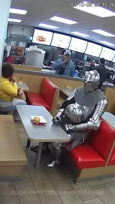 Knight in full armor sitting in a fast-food booth, struggling to eat a burger.