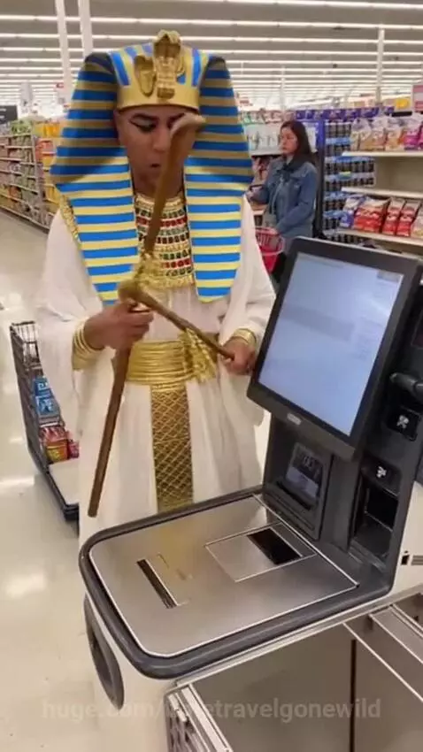 Man in Egyptian Pharaoh costume with headdress and staff arguing with a self-checkout machine in a grocery store.
