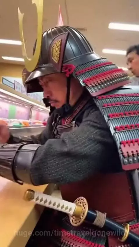 Man in samurai armor sitting at a sushi conveyor belt, eating with chopsticks.