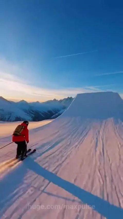 Skier performing an epic jump off a snow ramp with golden hour light on snow-capped mountains.