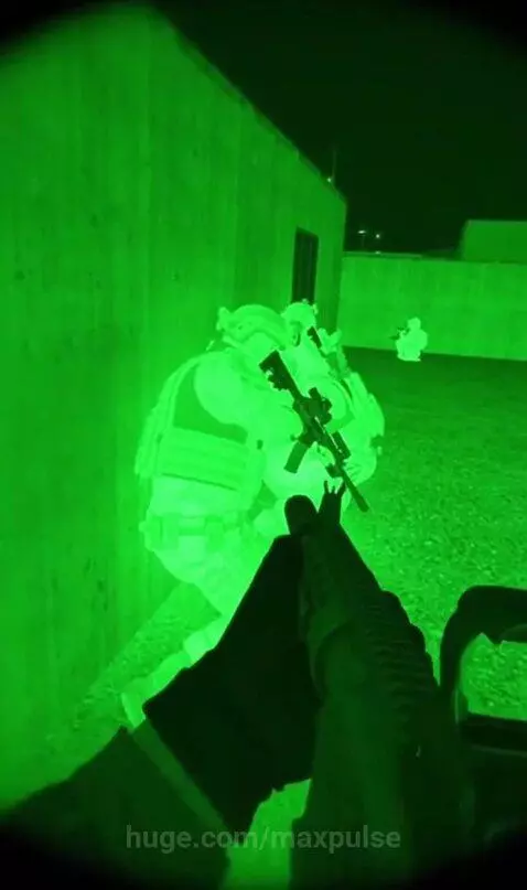 First-person view through night vision goggles, showing armored soldiers near a concrete wall and a distant figure.