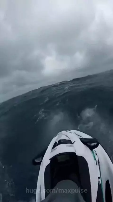 First-person view of a jet ski cutting through large, choppy waves under an overcast sky.