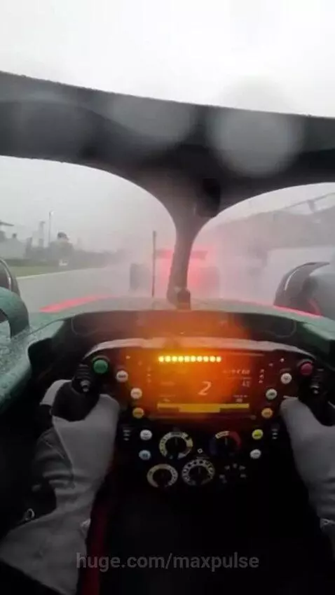 First-person view from an F1 cockpit on a rainy race track, showing raindrops on the windshield and spray from other cars.