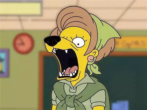 Cartoon character with dog features, black snout, fangs, and dog ears, mouth open in a bark, wearing a green shirt and headscarf in a classroom.
