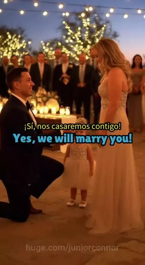 Man proposes to woman with daughter holding microphone between them during an outdoor evening event.