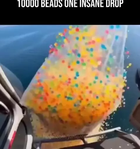 Thousands of colorful water beads exploding into a rainbow pattern upon hitting the ocean surface after being dropped from a helicopter.