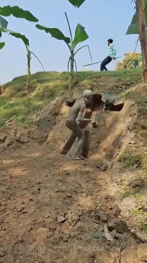 Man covered in mud lying in a ditch on a dirt hill as friends approach with shovels.