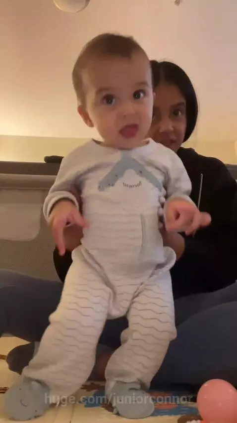 Baby in a light-colored striped shark onesie dancing while being held by an adult.