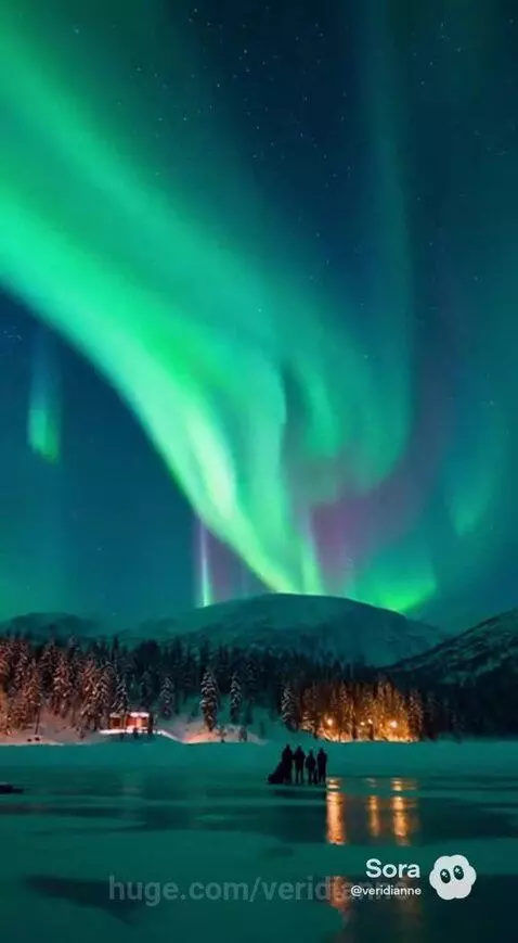 Spectacular Northern Lights display with green and purple hues over a snowy mountain landscape and frozen lake.
