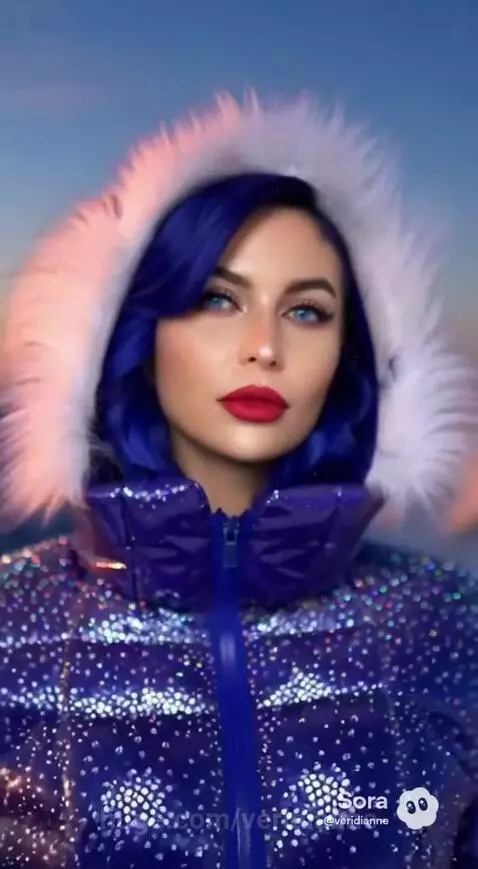 Woman with blue hair and a white fox on a snowy mountain ridge at sunset.