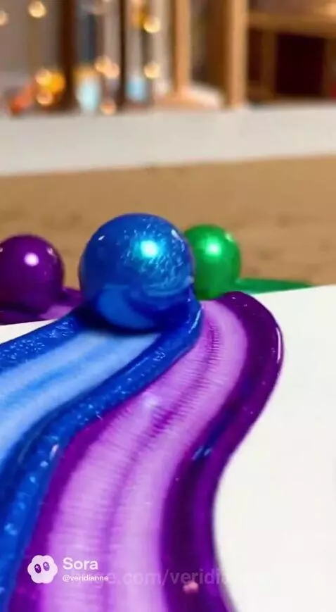 Blue, purple, and green marbles rolling through thick paint, creating beautiful, wavy patterns on a white surface.