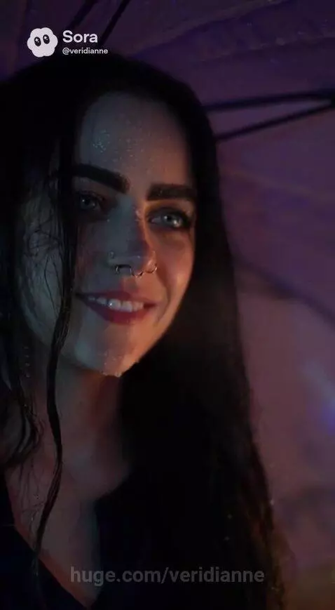 Woman with long dark hair and a purple umbrella smiles in a wet city street at night, with colorful reflections.