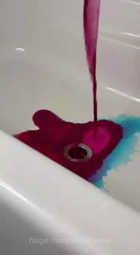 Close-up of brightly colored liquids swirling and mixing as they flow down a white bathtub drain.