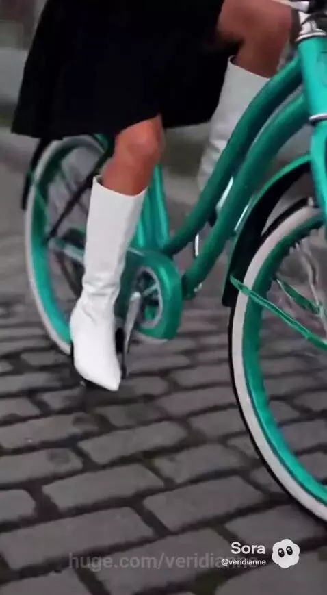 Woman with vibrant blue hair riding a turquoise bicycle through a black and white village with chickens.