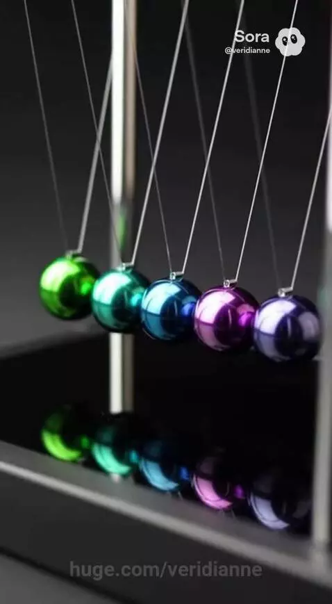 Newton's Cradle with five colorful metallic spheres suspended by strings, in motion, with reflections on a dark surface.