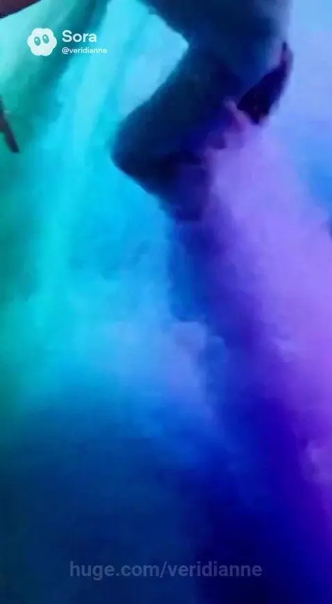 Woman in a blue and green sequined bodysuit and sheer top dances gracefully in colorful blue, turquoise, and purple smoke.