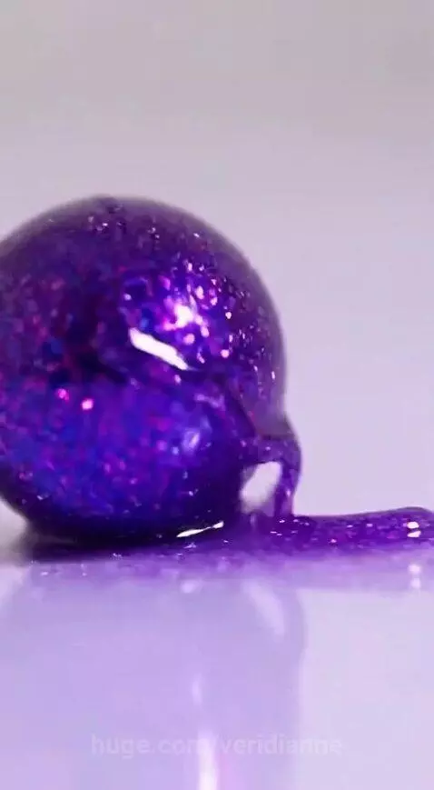 Close-up of vibrant purple glitter paint slowly spreading and shimmering on a light surface.