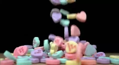 Close-up of pastel conversation heart candies with messages falling onto a black surface.